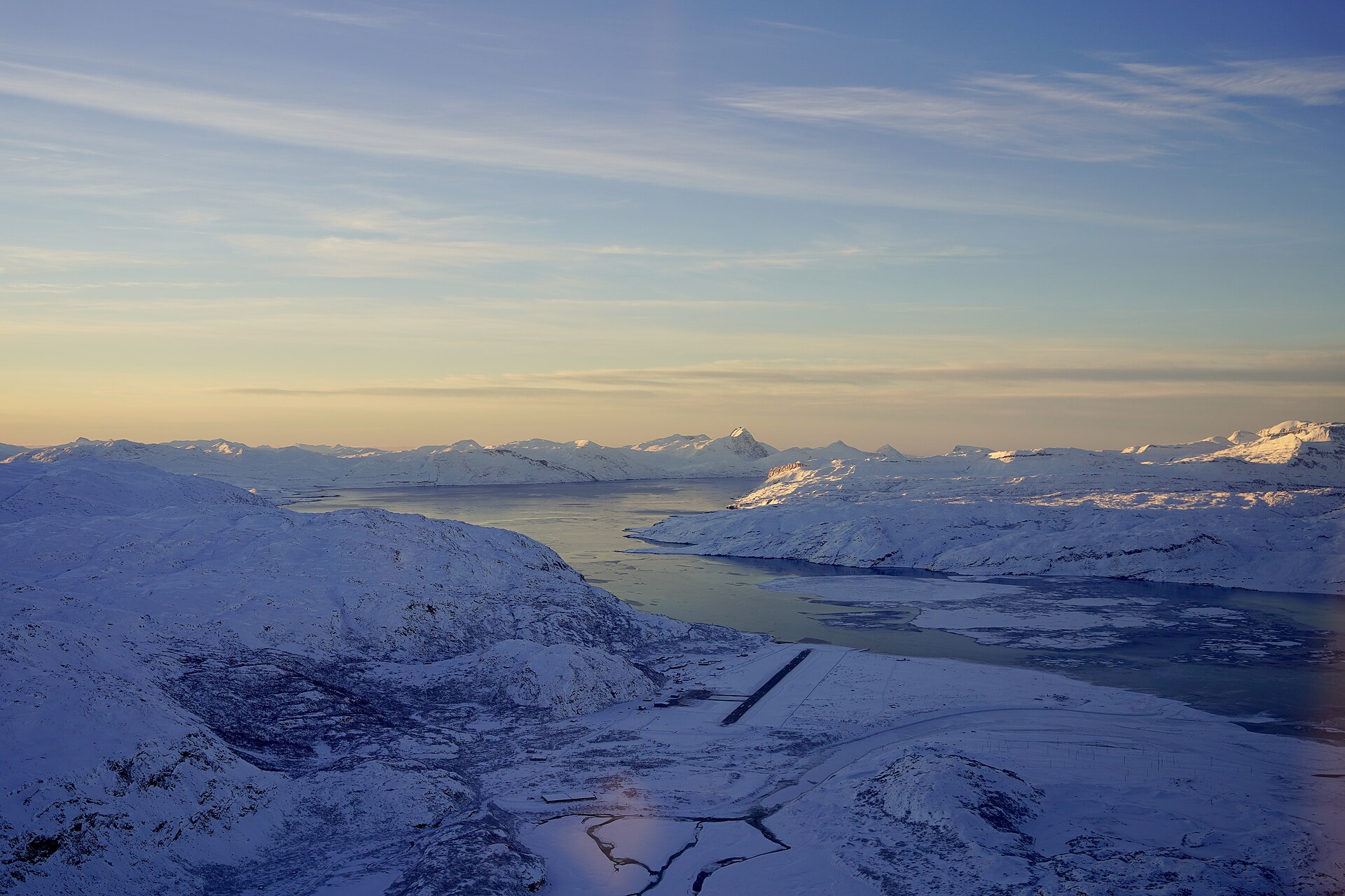 Snow-covered Narsarsuaq Airport runway beside a fjord and mountains